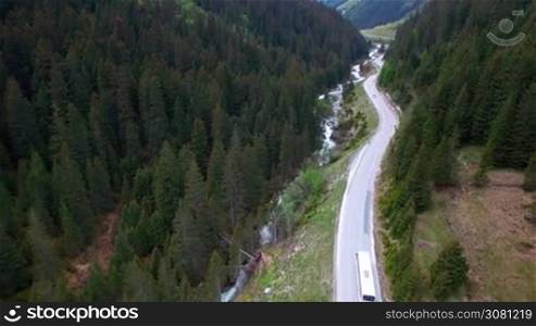 Aerial view of driving white color bus by a road in a mountainous area between the pine forest in Austria