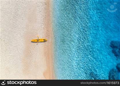 Aerial view of empty sandy beach with yellow canoe, sea coast with transparent blue water in sunny bright day in summer. Travel in Croatia. Top view of boats. Landscape with kayaks at sunset. Travel