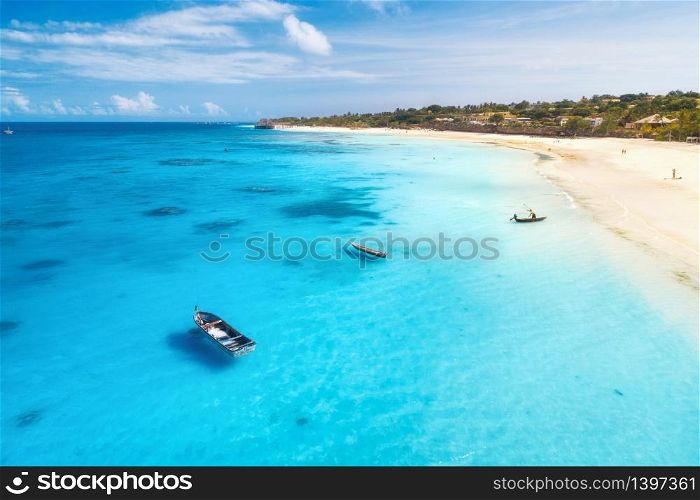 Aerial view of fishing boats and yachts on tropical sea coast with sandy beach at sunset in summer. Indian Ocean in Zanzibar. Top view of boat, palm trees, sky, clear blue water. View from above. Aerial view of boats and yachts on tropical sea coast in summer