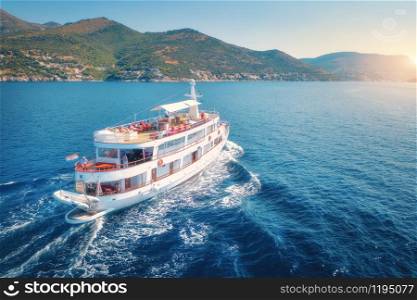 Aerial view of floating boat with relaxing people in blue sea at bright sunny summer evening. Adriatic sea in Croatia. Landscape with yacht, mountains, transparent blue water, sky at sunset. Top view