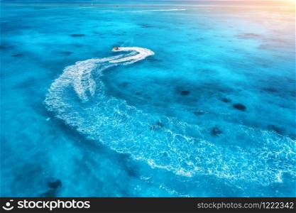 Aerial view of floating water scooter in blue water at sunset in summer. Holiday in Indian ocean, Zanzibar, Africa. Top view of jet ski in motion. Tropical seascape with moving motorboat. Extreme