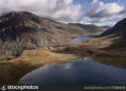 Aerial view of flying drone Epic early Autumn Fall landscape image of view along Ogwen vslley in Snowdonia National Park with dramatic sky and mountains
