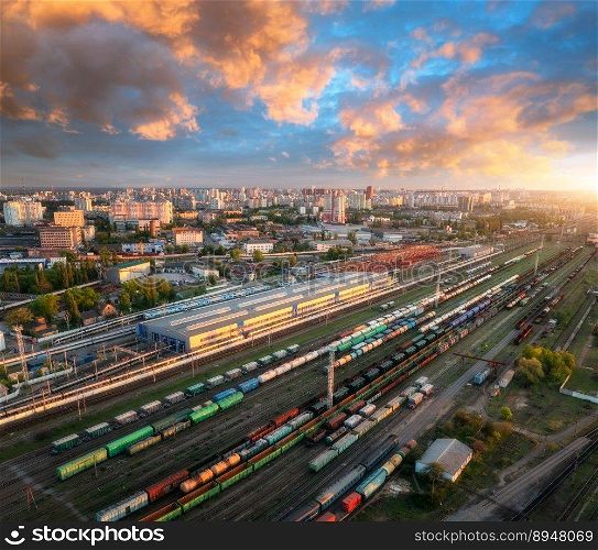 Aerial view of freight trains at sunset. Colorful railway cargo wagons on railroad. Drone view of colorful wagons, city, blue sky with clouds. Depot of freight trains. Railway station. Transportation. Aerial view of freight trains at sunset. Railway cargo wagons