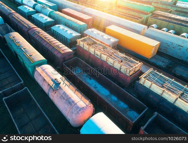 Aerial view of freight trains. Colorful cargo wagons on railway station. Wagons with goods on railroad. Heavy industry. Industrial landscape with train, railway platfform at sunset. Top view. Depot. Aerial view of freight trains. Cargo wagons on railway station