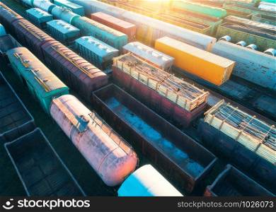 Aerial view of freight trains. Colorful cargo wagons on railway station. Wagons with goods on railroad. Heavy industry. Industrial landscape with train, railway platfform at sunset. Top view. Depot. Aerial view of freight trains. Cargo wagons on railway station