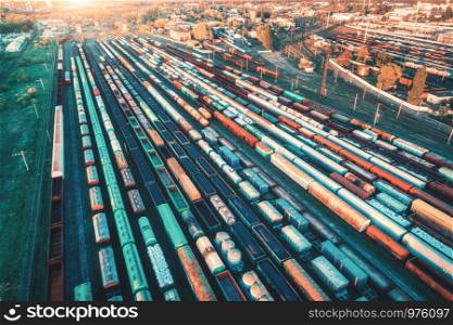 Aerial view of freight trains. Colorful cargo wagons on railway station. Wagons with goods on railroad. Heavy industry. Industrial landscape with train, railway platfform at sunset. Top view. Depot