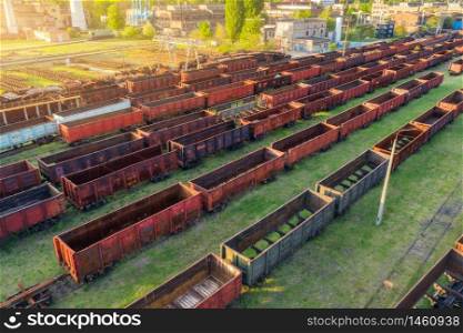 Aerial view of freight trains. Top view of old rusty wagons on railroad. Heavy industry. Industrial landscape with train, green trees and grass at sunset in summer. Railway station. Transportation