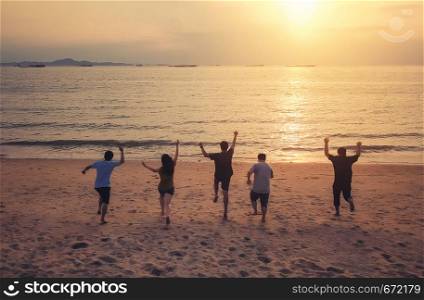 Aerial view of friends running on the beach or sea together and celebrating on holiday or vacation in party in summer at sunset time