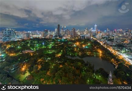 Aerial view of green trees in Lumpini Park, Sathorn district, Bangkok Downtown Skyline. Thailand. Financial district and business center in smart urban city in Asia. Skyscraper buildings at night.