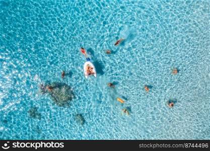 Aerial view of happy people swimming in blue sea at sunset in summer. Vacation in Sardinia, Italy. Top down view of clear azure water, sandy beach, boat. Colorful tropical landscape. Travel. Concept