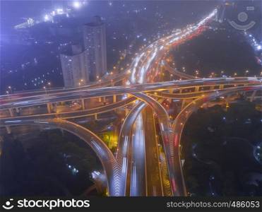 Aerial view of highway junctions shape letter x cross at night with fog. Bridges, roads, or streets in transportation concept. Structure shapes of architecture in urban city, Shanghai Downtown, China.