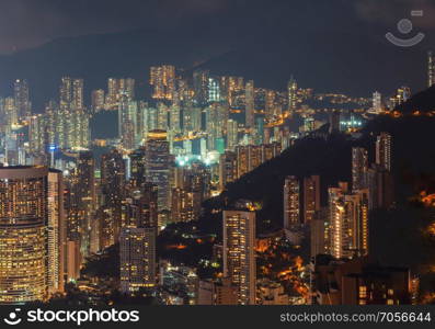 Aerial view of Hong Kong apartments and mountain in cityscape background. Residential district in smart city in Asia. Buildings at night.