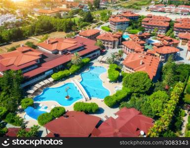 Aerial view of hotel, pool, swimming people in transparent blue water, umbrellas, sunbeds, green trees at sunset. Summer holidays. Top view of buildings. Relax and leisure in luxury resort in Europe