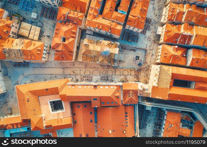 Aerial view of houses with orange roofs at sunset in summer in Dubrovnik, Croatia. Top view of beautiful architecture in old city. Historical centre, buildings, walking people on the street. Travel