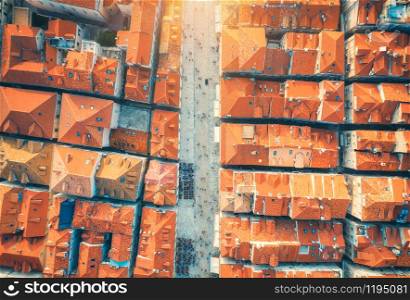 Aerial view of houses with orange roofs at sunset in summer in Dubrovnik, Croatia. Top view of beautiful architecture in old city. Historical centre, buildings, walking people on the street. Travel