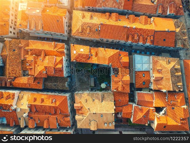 Aerial view of houses with orange roofs at sunset in summer in Dubrovnik, Croatia. Top view of beautiful architecture in european old city. Historical centre, buildings, street in the evening. Travel