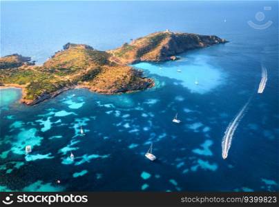 Aerial view of island, sea bay with clear azure water, yachts and boats on blue sea at sunset in summer. Sardinia, Italy. Tropical seascape with speed boats, mountain, ocean. Top drone view