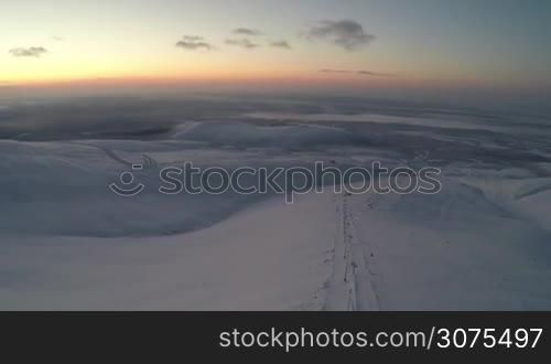 Aerial view of Khibiny mountains, Russia in twilight. There is a ski-lift on the slope, man is driving the snowmobile