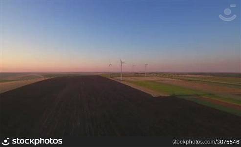 Aerial view of large wind turbines in a wind farm at sunset, producing sustainable and renewable energy.