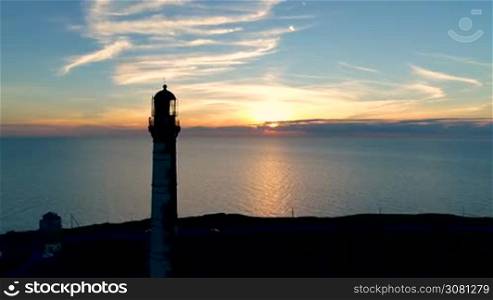 Aerial view of Lighthouse on a sunset background in the sea in summer. Flying of the drone past the lighthouse at sunset
