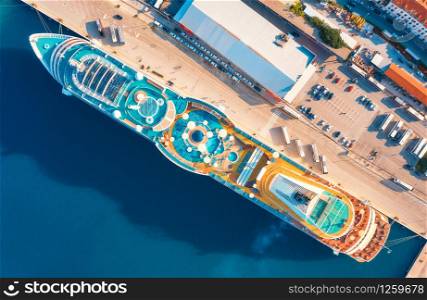 Aerial view of luxury cruise liner in port. Top view of swimming pool with sunbeds, umbrellas and deck chairs, wooden deck on the cruise ship, cars and buildings in summer. View from above. Resort