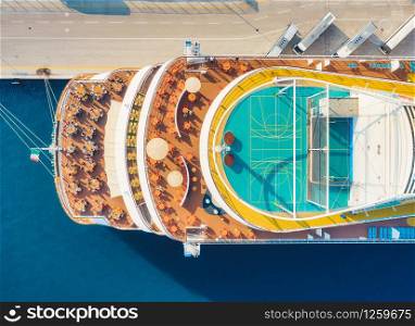 Aerial view of luxury cruise liner. Top view of basketball field, people is sitting at the tables, umbrellas on the cruise ship in summer. View from above of restaurant on the wooden deck. Resort