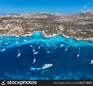 Aerial view of luxury yachts and boats on blue sea at summer sunny day. Travel in Sardinia, Italy. Drone view from above of speed boats, yachts, sea bay, rocky coast, transparent water. Seascape