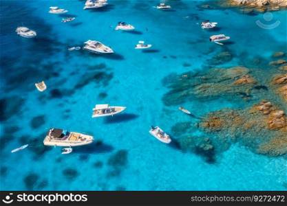 Aerial view of luxury yachts and boats on blue sea at summer sunny day. Travel in Sardinia, Italy. Drone view from above of speed boats, yachts, sea bay, rocky coast, transparent water. Seascape