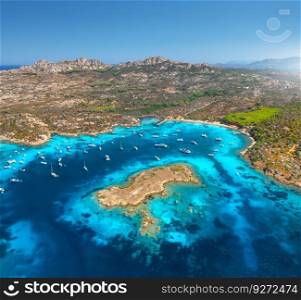 Aerial view of luxury yachts and boats on blue sea at summer sunny day. Travel in Sardinia, Italy. Drone view from above of sea bay, mountain, small island, rocky coast, transparent water. Seascape
