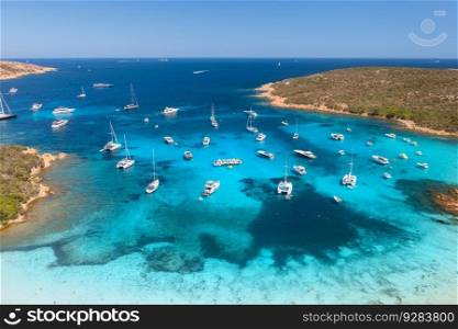 Aerial view of luxury yachts and boats on sea bay at sunset in summer. Travel in Sardinia, Italy. Drone view from above of speed boats, yachts, sea lagoon, rocky coast, transparent water. Seascape