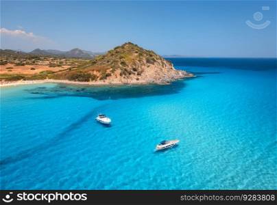 Aerial view of luxury yachts on blue sea at sunset in summer. Sardinia, Italy. Tropical seascape with speed boats, yachts, sea lagoon, mountain, ocean with transparent azure water, sky. Top drone view