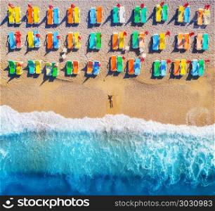 Aerial view of lying woman on the beach with colorful chaise-lounges. Young woman on the sea at sunset in Oludeniz, Turkey. Top view. Seascape with girl on the seashore, blue water and waves. Holiday. Aerial view of lying woman on the beach with colorful chaise-lounges