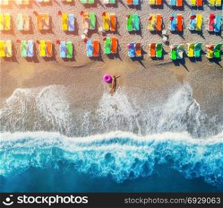 Aerial view of lying woman with swim ring in the sea in Oludeniz, Turkey. Summer seascape with girl, blue water, waves and sandy beach with colorful chaise-lounges at sunset. Top view from drone . Aerial view of lying woman with swim ring in the sea