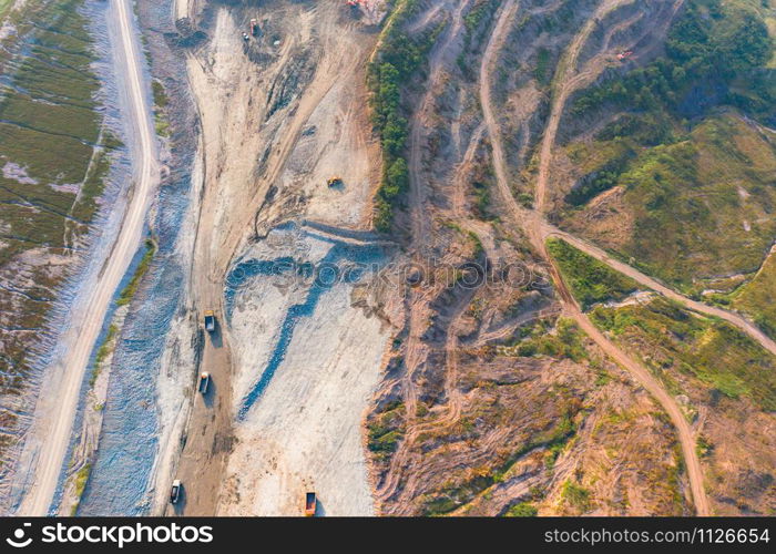 Aerial view of machine excavator trucks dig coal mining or ore with black grunge ground in quarry with mountain hills. Nature landscape background in factory industry. Environment resources