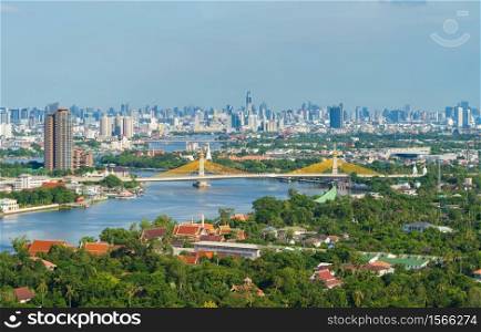 Aerial view of Maha Chesadabodindranusorn Bridge or Nonthaburi Bridge crossing Chao Phraya River and Bangkok skyline, Thailand. Urban city and downtown with skyscraper buildings.