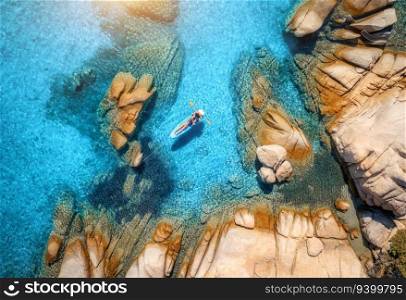 Aerial view of man on sup board in blue sea, rocks at sunrise in summer. Man on floating canoe in transparent azure water. Kayak. Sardinia island, Italy. Tropical seascape. Active travel. Top view
