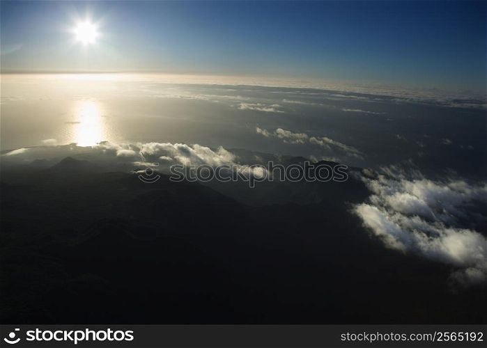 Aerial view of Maui, Hawaii coast with sun over Pacific ocean and mountainous landscape.