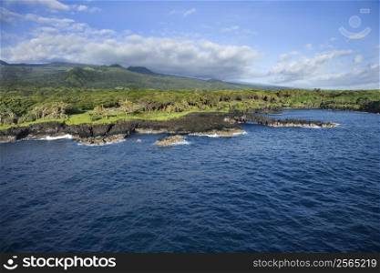 Aerial view of Maui, Hawaii landscape with Pacific ocean coastline and rocky cliffs with mountains in background.