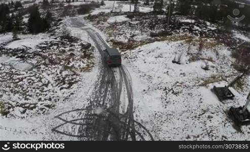 Aerial view of minivan driving along snowy rural road in the northern town. Living in severe climate