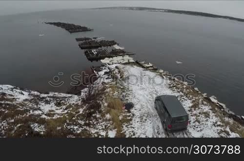 Aerial view of minivan standing by waterside with unfinished bridge with following view to the Rabocheostrovsk, township on the White Sea coast near Solovki
