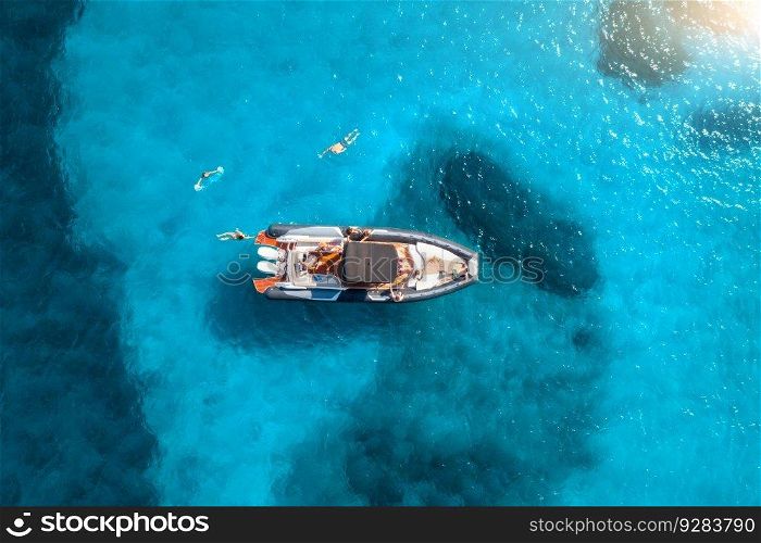 Aerial view of motorboat and swimming people in blue sea at sunset in summer. Sardinia, Italy. Top drone view of yacht, ocean, transparent azure water. Travel. Tropical landscape. Yachting. Seascape
