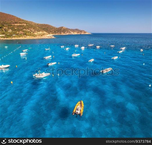 Aerial view of motorboats on blue sea at sunset in summer. Sardinia, Italy. Tropical seascape with speed boats, yachts, sea lagoon, mountain, transparent azure water, sky. Top drone view of ocean