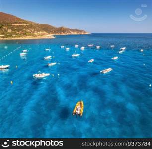 Aerial view of motorboats on blue sea at sunset in summer. Sardinia, Italy. Tropical seascape with speed boats, yachts, sea lagoon, mountain, transparent azure water, sky. Top drone view of ocean