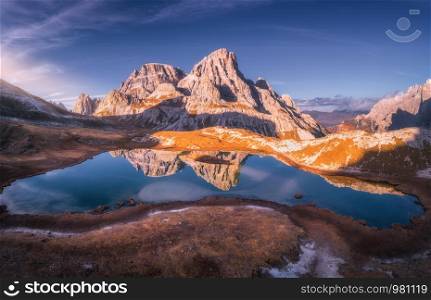 Aerial view of mountain lake with reflection at sunset in autumn. Landscape with purple sky, mountains, hills with grass, blue water in fall. Top view of high rocks. Beautiful nature. Dolomites, Italy. Aerial view of mountain lake with reflection at sunset in autumn