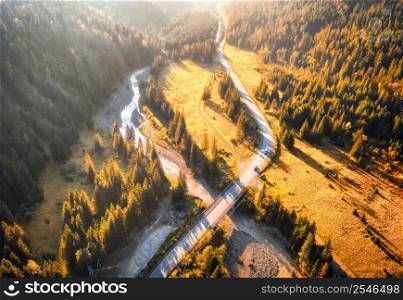 Aerial view of mountain road and beautiful forest at sunset in autumn. Carpathians, Ukraine. Top view from drone of road, bridge, woods, cars, green meadows and river. Roadway in fall. Travel