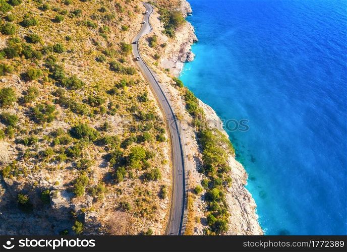 Aerial view of mountain road, cars, blue sea with sandy beach at sunset in summer. Oludeniz, Turkey. Top view of road, trees, clear water, mountain. Beautiful landscape with highway, rocks, sea coast