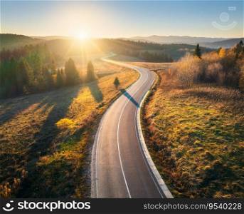 Aerial view of mountain road in forest at sunset in autumn in Ukraine. Top drone view of road in woods. Beautiful landscape with roadway in hills, pine trees, meadows, golden sunlight in fall. Travel