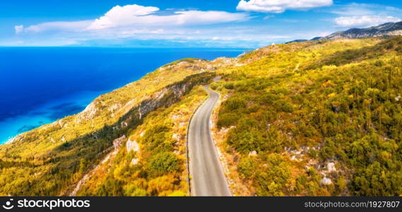 Aerial view of mountain road near blue sea, forest, sky with clouds at sunset in autumn. Lefkada, Greece. Top view of road, orange trees, hills in fall. Beautiful landscape with highway and sea coast