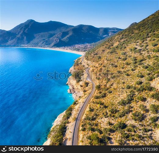 Aerial view of mountain road near blue sea, sandy beach at sunset in summer. Oludeniz, Turkey. Top view of road, trees, clear water, mountain. Beautiful landscape with highway, rocks and sea coast