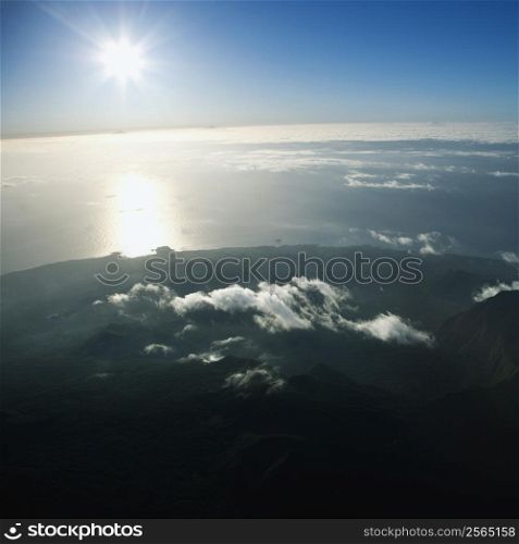 Aerial view of mountainous terrain in Maui, Hawaii with sun shining off the Pacific ocean in background.